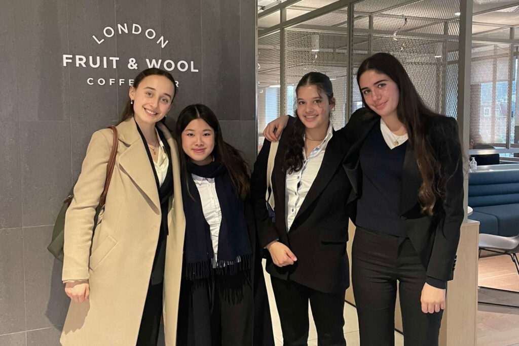 4 girls stood in suits at a law firm smiling at the camera with their arms around each other looking happy