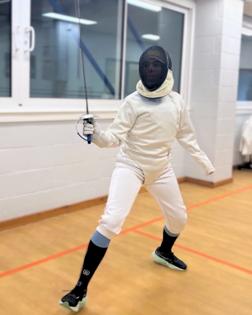 girl fencing in a sports hall on a fencing piste dressed in classic white fencing gear lunging forward