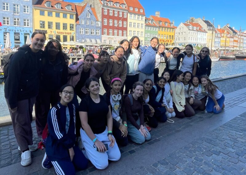 Group of girls stood in front of multicoloured houses smiling at the camera